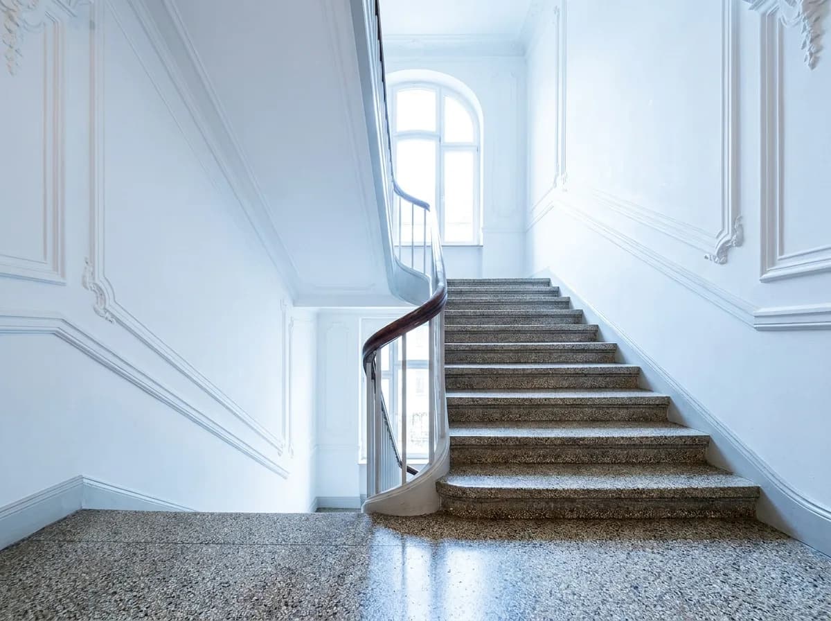 Frisch gereinigtes Altbau-Treppenhaus mit geschwungenem Holzhandlauf und Terrazzoboden